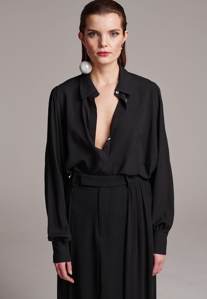 Voluminous poplin shirt with puffed subtle gathered shoulders. Specially detailed with a square armhole seam to create a voluminous sleeve. It has six-hole buttons to adjust the neckline. Cut from 100% silk. Designed for a relaxed fit, cut to be worn very loose. Embellished with a faux pearl on the cuff. This style will go hand in hand with jeans and tailoring.