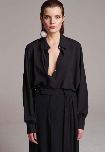 Voluminous poplin shirt with puffed subtle gathered shoulders. Specially detailed with a square armhole seam to create a voluminous sleeve. It has six-hole buttons to adjust the neckline. Cut from 100% silk. Designed for a relaxed fit, cut to be worn very loose. Embellished with a faux pearl on the cuff. This style will go hand in hand with jeans and tailoring.