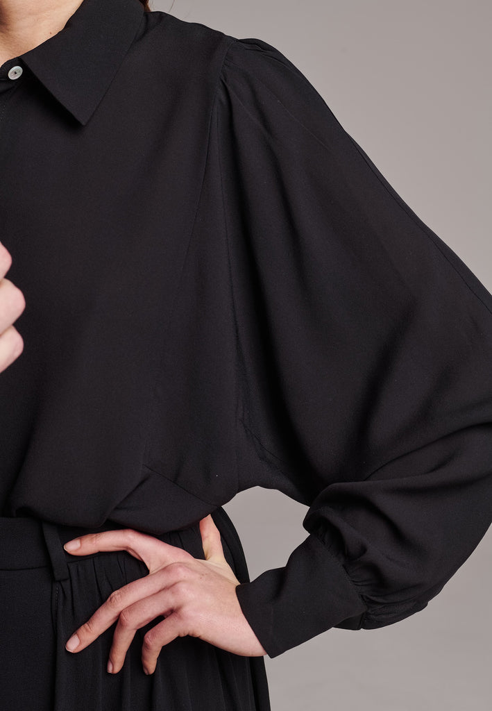 Voluminous poplin shirt with puffed subtle gathered shoulders. Specially detailed with a square armhole seam to create a voluminous sleeve. It has six-hole buttons to adjust the neckline. Cut from 100% silk. Designed for a relaxed fit, cut to be worn very loose. Embellished with a faux pearl on the cuff. This style will go hand in hand with jeans and tailoring.