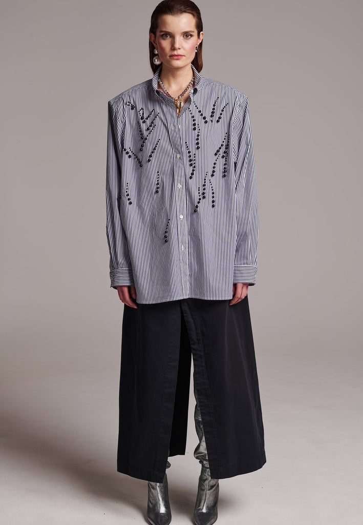 FRENKEN manages to create designs that are somehow classic yet totally modern at the same time. This oversized very easy-to-wear menswear shirt is a true homage to the eighties cut Ralph Lauren men's shirt. Dropped shoulders, with adjustable shoulder pads. Detailed with a mirrored F. Cut from 100% cotton poplin. This Ralf shirt is embellished with faux pearls in an increasing from small to large formation. It's an asset to your wardrobe.