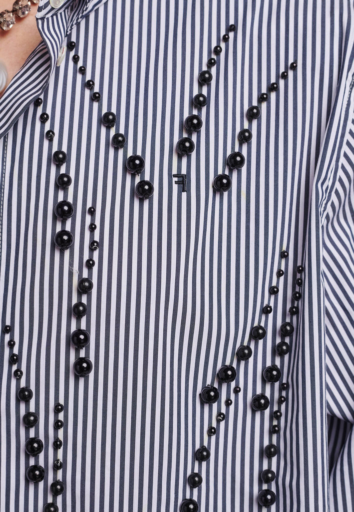 FRENKEN manages to create designs that are somehow classic yet totally modern at the same time. This oversized very easy-to-wear menswear shirt is a true homage to the eighties cut Ralph Lauren men's shirt. Dropped shoulders, with adjustable shoulder pads. Detailed with a mirrored F. Cut from 100% cotton poplin. This Ralf shirt is embellished with faux pearls in an increasing from small to large formation. It's an asset to your wardrobe.