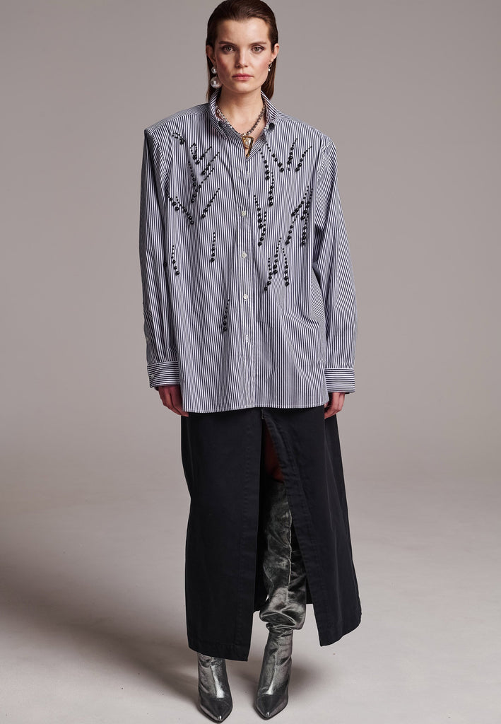 FRENKEN manages to create designs that are somehow classic yet totally modern at the same time. This oversized very easy-to-wear menswear shirt is a true homage to the eighties cut Ralph Lauren men's shirt. Dropped shoulders, with adjustable shoulder pads. Detailed with a mirrored F. Cut from 100% cotton poplin. This Ralf shirt is embellished with faux pearls in an increasing from small to large formation. It's an asset to your wardrobe.
