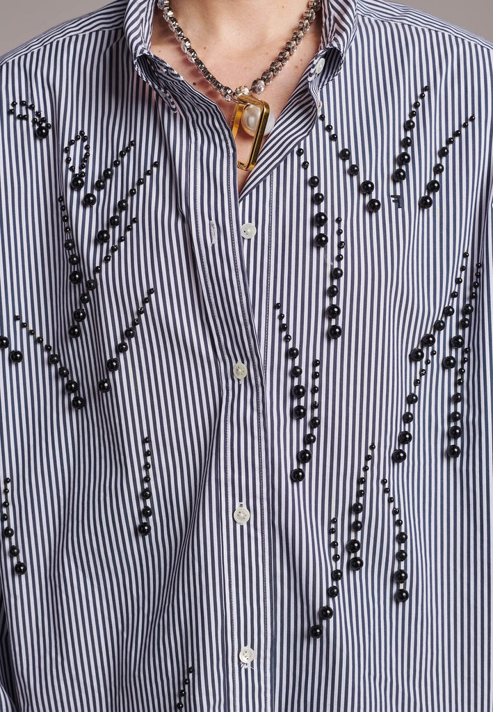 FRENKEN manages to create designs that are somehow classic yet totally modern at the same time. This oversized very easy-to-wear menswear shirt is a true homage to the eighties cut Ralph Lauren men's shirt. Dropped shoulders, with adjustable shoulder pads. Detailed with a mirrored F. Cut from 100% cotton poplin. This Ralf shirt is embellished with faux pearls in an increasing from small to large formation. It's an asset to your wardrobe.