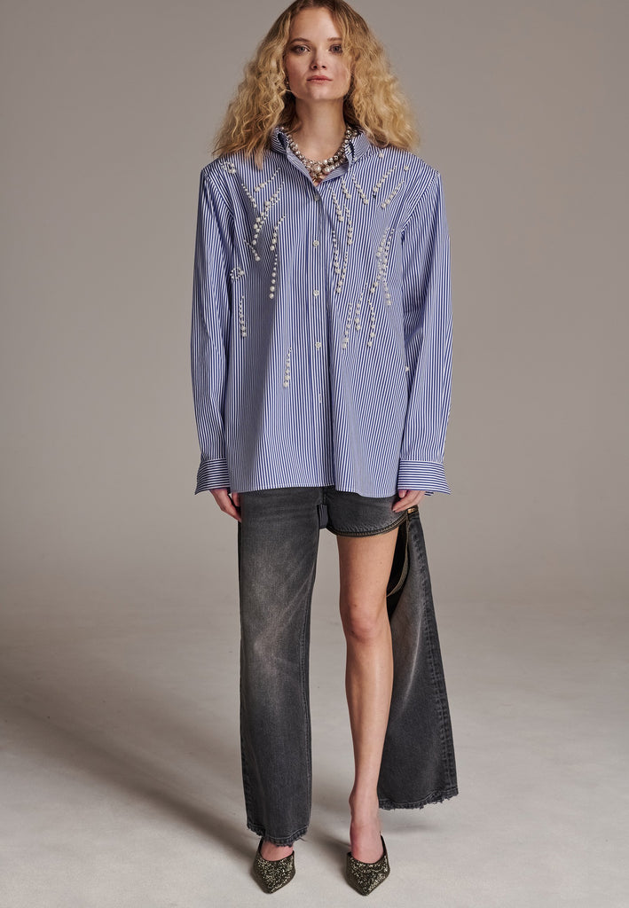 FRENKEN manages to create designs that are somehow classic yet totally modern at the same time. This oversized very easy-to-wear menswear shirt is a true homage to the eighties cut Ralph Lauren men's shirt. Dropped shoulders, with adjustable shoulder pads. Detailed with a mirrored F. Cut from 100% cotton poplin. This Ralf shirt is embellished with faux pearls in an increasing from small to large formation. It's an asset to your wardrobe.