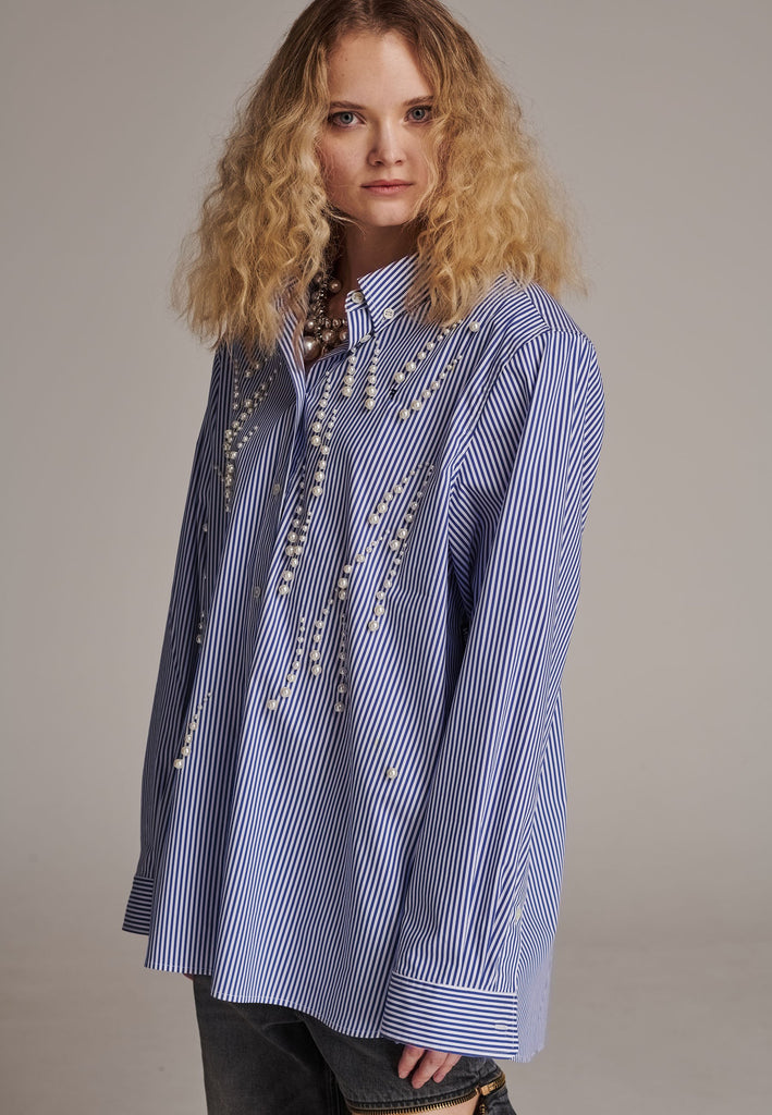 FRENKEN manages to create designs that are somehow classic yet totally modern at the same time. This oversized very easy-to-wear menswear shirt is a true homage to the eighties cut Ralph Lauren men's shirt. Dropped shoulders, with adjustable shoulder pads. Detailed with a mirrored F. Cut from 100% cotton poplin. This Ralf shirt is embellished with faux pearls in an increasing from small to large formation. It's an asset to your wardrobe.