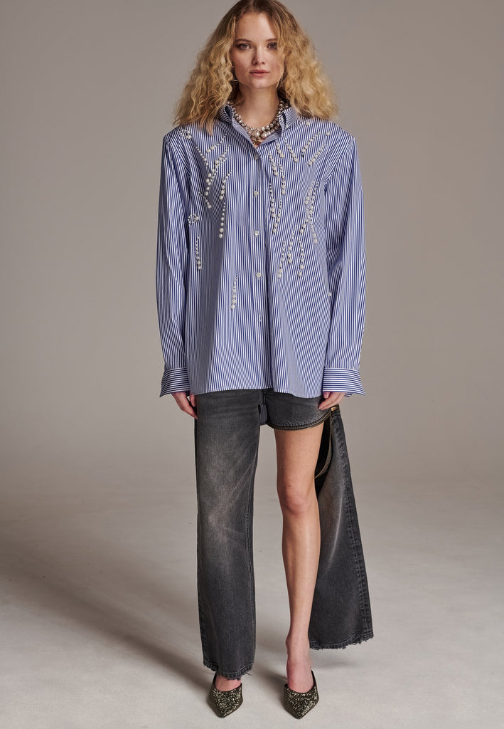 FRENKEN manages to create designs that are somehow classic yet totally modern at the same time. This oversized very easy-to-wear menswear shirt is a true homage to the eighties cut Ralph Lauren men's shirt. Dropped shoulders, with adjustable shoulder pads. Detailed with a mirrored F. Cut from 100% cotton poplin. This Ralf shirt is embellished with faux pearls in an increasing from small to large formation. It's an asset to your wardrobe.