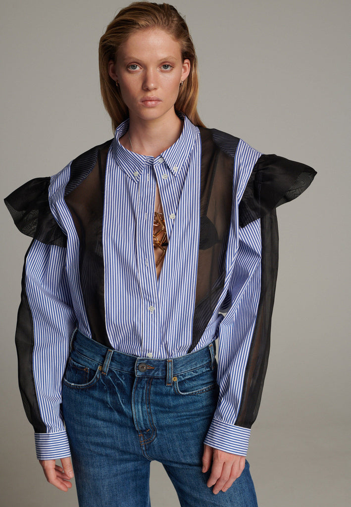 The oversized fit offers comfort and versatility, and also combines modern edge with a touch of elegance. Designed with sheer transparent panels, it adds a subtle, stylish contrast to the solid fabric. Ruffled details on the shoulders enhance its playful, feminine appeal while maintaining a relaxed, contemporary vibe.