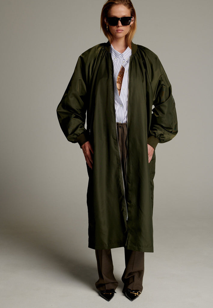 This long bomber jacket offers a perfect blend of modern style and functionality. It features two distinctive zipper closures—one in silver and the other in gold—on the sleeve, adding a bold, metallic contrast and unique detail. The elongated silhouette provides a sleek, urban look, while the durable nylon material ensures warmth and comfort.
