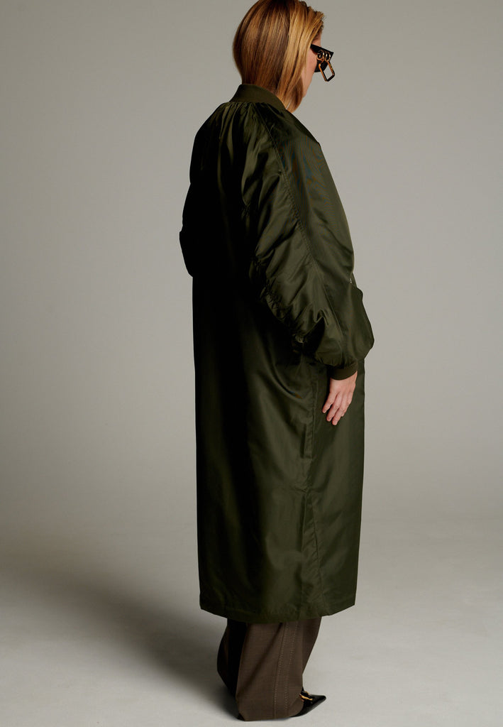 This long bomber jacket offers a perfect blend of modern style and functionality. It features two distinctive zipper closures—one in silver and the other in gold—on the sleeve, adding a bold, metallic contrast and unique detail. The elongated silhouette provides a sleek, urban look, while the durable nylon material ensures warmth and comfort.
