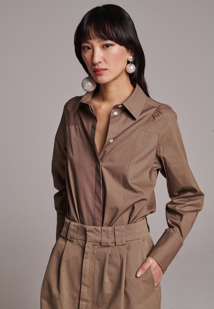 Poplin shirt cut for a relaxed fit with subtle puffed shoulder and some fine gathering. Special detailed with a square armhole seam. It has six-hole buttons to adjust the neckline. Cut from crispy 100% poplin. Embellished with a faux pearl on the left cuff. This style will go hand in hand with garment-dyed skirts and tailoring.