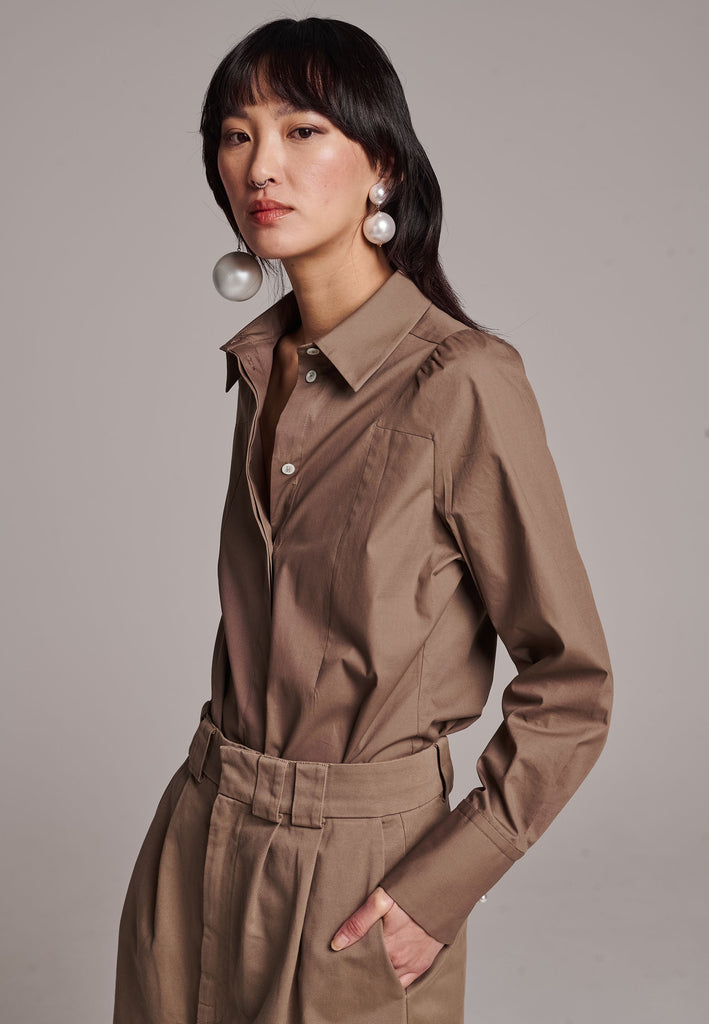 Poplin shirt cut for a relaxed fit with subtle puffed shoulder and some fine gathering. Special detailed with a square armhole seam. It has six-hole buttons to adjust the neckline. Cut from crispy 100% poplin. Embellished with a faux pearl on the left cuff. This style will go hand in hand with garment-dyed skirts and tailoring.