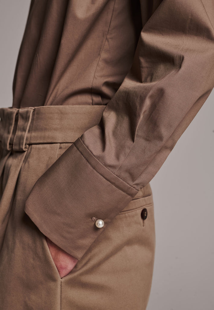 Poplin shirt cut for a relaxed fit with subtle puffed shoulder and some fine gathering. Special detailed with a square armhole seam. It has six-hole buttons to adjust the neckline. Cut from crispy 100% poplin. Embellished with a faux pearl on the left cuff. This style will go hand in hand with garment-dyed skirts and tailoring.