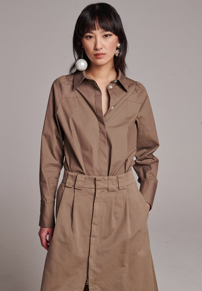 Poplin shirt cut for a relaxed fit with subtle puffed shoulder and some fine gathering. Special detailed with a square armhole seam. It has six-hole buttons to adjust the neckline. Cut from crispy 100% poplin. Embellished with a faux pearl on the left cuff. This style will go hand in hand with garment-dyed skirts and tailoring.