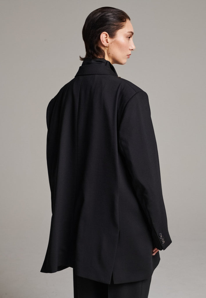 A classic yet oversized blazer, designed to make a bold statement while maintaining timeless appeal. The lower portion of the lapels is crafted from a contrasting shiny fabric, adding an unexpected touch of texture and luxury. The upper part of the collar area is beautifully embellished with gold and silver rings at the tips, offering a refined, modern twist. This piece combines traditional tailoring with avant-garde details, perfect for elevating any outfit with sophistication and edge.