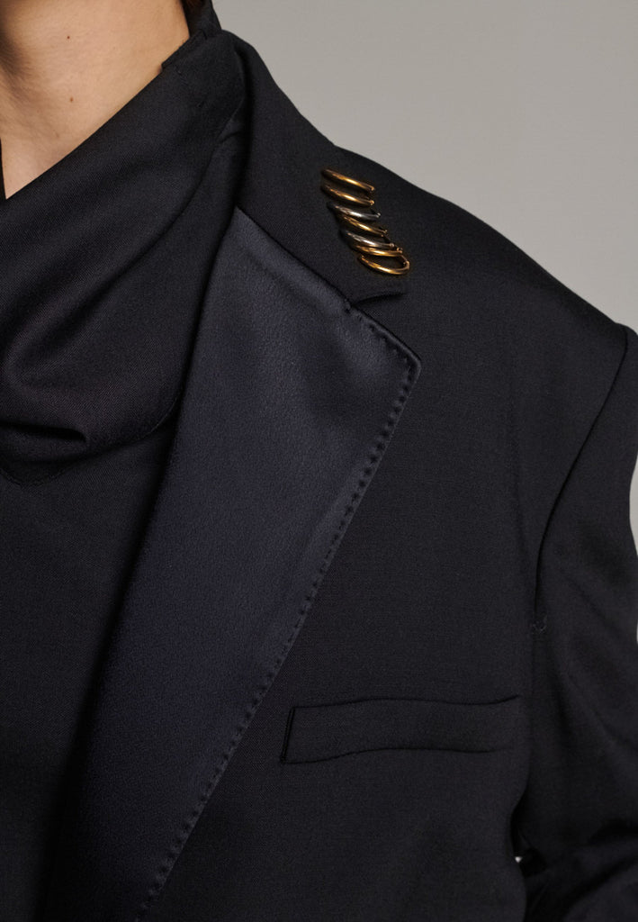 A classic yet oversized blazer, designed to make a bold statement while maintaining timeless appeal. The lower portion of the lapels is crafted from a contrasting shiny fabric, adding an unexpected touch of texture and luxury. The upper part of the collar area is beautifully embellished with gold and silver rings at the tips, offering a refined, modern twist. This piece combines traditional tailoring with avant-garde details, perfect for elevating any outfit with sophistication and edge.