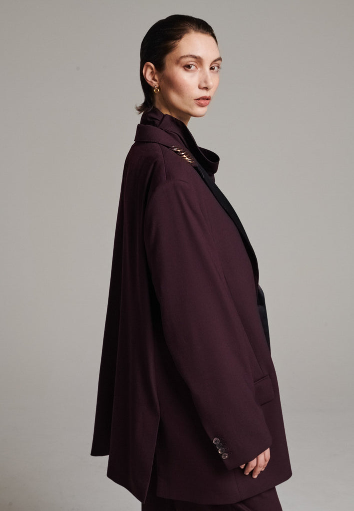 A classic yet oversized blazer, designed to make a bold statement while maintaining timeless appeal. The lower portion of the lapels is crafted from a contrasting shiny fabric, adding an unexpected touch of texture and luxury. The upper part of the collar area is beautifully embellished with gold and silver rings at the tips, offering a refined, modern twist. This piece combines traditional tailoring with avant-garde details, perfect for elevating any outfit with sophistication and edge.