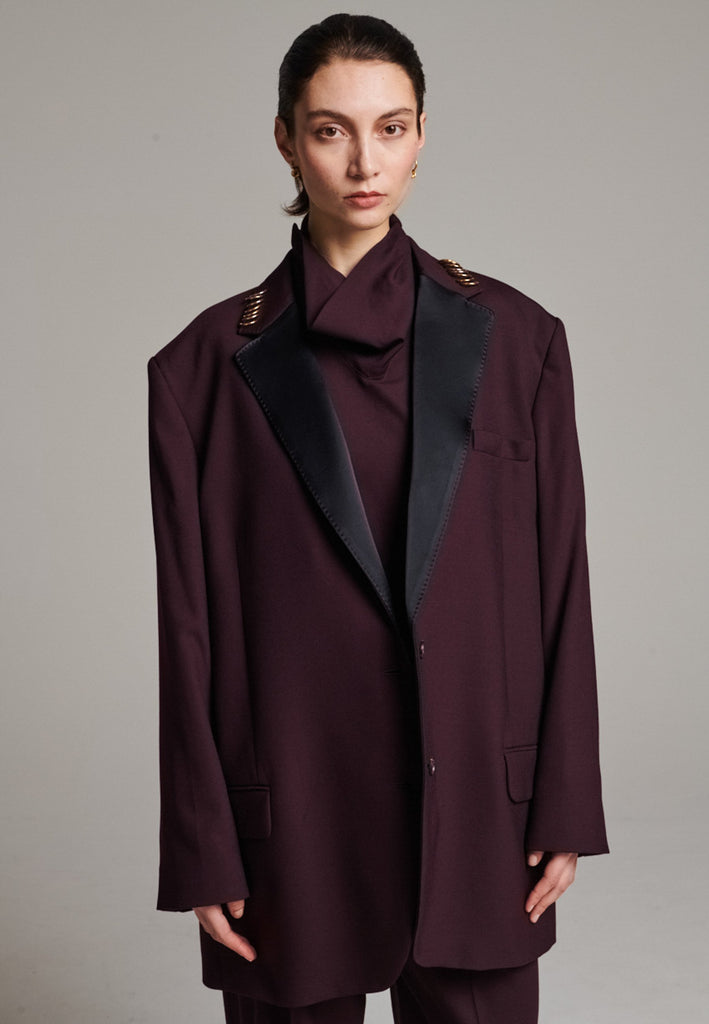 A classic yet oversized blazer, designed to make a bold statement while maintaining timeless appeal. The lower portion of the lapels is crafted from a contrasting shiny fabric, adding an unexpected touch of texture and luxury. The upper part of the collar area is beautifully embellished with gold and silver rings at the tips, offering a refined, modern twist. This piece combines traditional tailoring with avant-garde details, perfect for elevating any outfit with sophistication and edge.