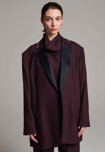 A classic yet oversized blazer, designed to make a bold statement while maintaining timeless appeal. The lower portion of the lapels is crafted from a contrasting shiny fabric, adding an unexpected touch of texture and luxury. The upper part of the collar area is beautifully embellished with gold and silver rings at the tips, offering a refined, modern twist. This piece combines traditional tailoring with avant-garde details, perfect for elevating any outfit with sophistication and edge.