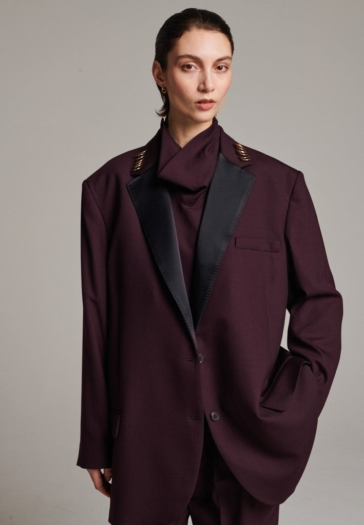 A classic yet oversized blazer, designed to make a bold statement while maintaining timeless appeal. The lower portion of the lapels is crafted from a contrasting shiny fabric, adding an unexpected touch of texture and luxury. The upper part of the collar area is beautifully embellished with gold and silver rings at the tips, offering a refined, modern twist. This piece combines traditional tailoring with avant-garde details, perfect for elevating any outfit with sophistication and edge.