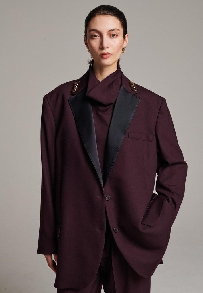 A classic yet oversized blazer, designed to make a bold statement while maintaining timeless appeal. The lower portion of the lapels is crafted from a contrasting shiny fabric, adding an unexpected touch of texture and luxury. The upper part of the collar area is beautifully embellished with gold and silver rings at the tips, offering a refined, modern twist. This piece combines traditional tailoring with avant-garde details, perfect for elevating any outfit with sophistication and edge.