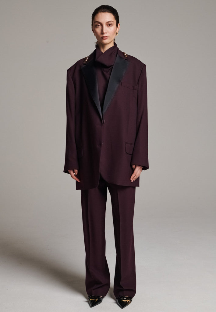 A classic yet oversized blazer, designed to make a bold statement while maintaining timeless appeal. The lower portion of the lapels is crafted from a contrasting shiny fabric, adding an unexpected touch of texture and luxury. The upper part of the collar area is beautifully embellished with gold and silver rings at the tips, offering a refined, modern twist. This piece combines traditional tailoring with avant-garde details, perfect for elevating any outfit with sophistication and edge.