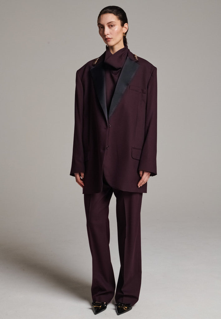 A classic yet oversized blazer, designed to make a bold statement while maintaining timeless appeal. The lower portion of the lapels is crafted from a contrasting shiny fabric, adding an unexpected touch of texture and luxury. The upper part of the collar area is beautifully embellished with gold and silver rings at the tips, offering a refined, modern twist. This piece combines traditional tailoring with avant-garde details, perfect for elevating any outfit with sophistication and edge.