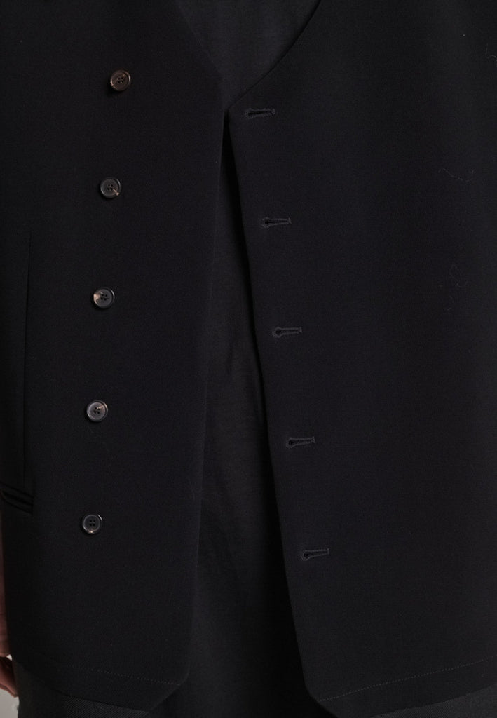 A bold reinterpretation of a classic vest silhouette, cut in a voluminous, oversized shape, it combines sharp tailoring with a contemporary twist. A standout feature is the exaggerated hem, crafted in a contrasting black fabric with a subtle sheen, adding depth and visual interest to the minimalist design. With its clean lines, deep armholes, and striking finish, this piece layers effortlessly and brings a refined edge to both casual and dressed-up looks.
