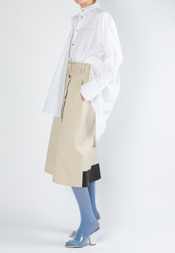Rubber skirt, sand color. A-line skirt made from trench cotton in light sand. Detailed with a rubber stripe at the back hem and fly-front horn button, closing with a slit and fabric-covered belt. 100% cotton