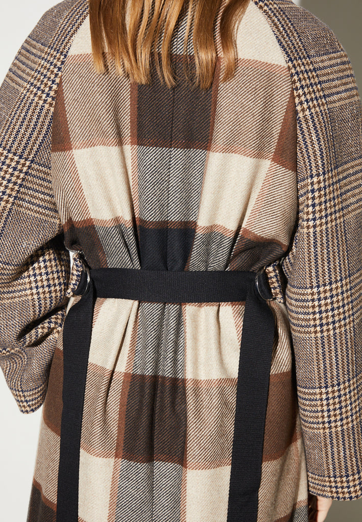 Reaction, an oversized raglan coat that combines two plaid fabrics in shades of brown, with front buttons and a D-ring strap tie that changes from the front to the back. This is the coat of the season, a total game-changer. You can style it with a tracking suit or with a working suit, either way, any look will feel complete with this statement coat.
