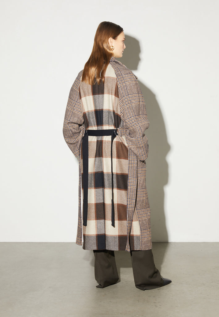Reaction, an oversized raglan coat that combines two plaid fabrics in shades of brown, with front buttons and a D-ring strap tie that changes from the front to the back. This is the coat of the season, a total game-changer. You can style it with a tracking suit or with a working suit, either way, any look will feel complete with this statement coat.