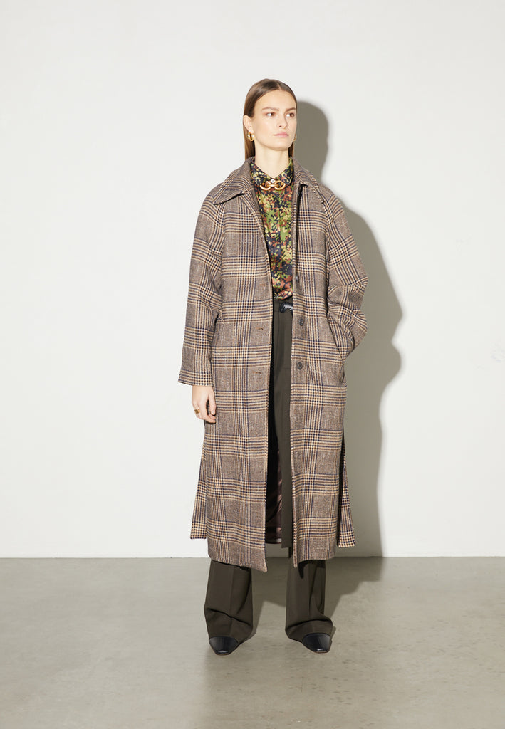 Reaction, an oversized raglan coat that combines two plaid fabrics in shades of brown, with front buttons and a D-ring strap tie that changes from the front to the back. This is the coat of the season, a total game-changer. You can style it with a tracking suit or with a working suit, either way, any look will feel complete with this statement coat.