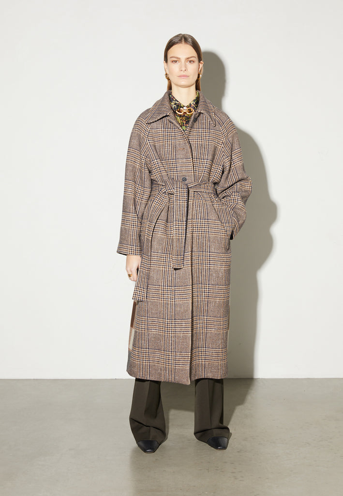 Reaction, an oversized raglan coat that combines two plaid fabrics in shades of brown, with front buttons and a D-ring strap tie that changes from the front to the back. This is the coat of the season, a total game-changer. You can style it with a tracking suit or with a working suit, either way, any look will feel complete with this statement coat.