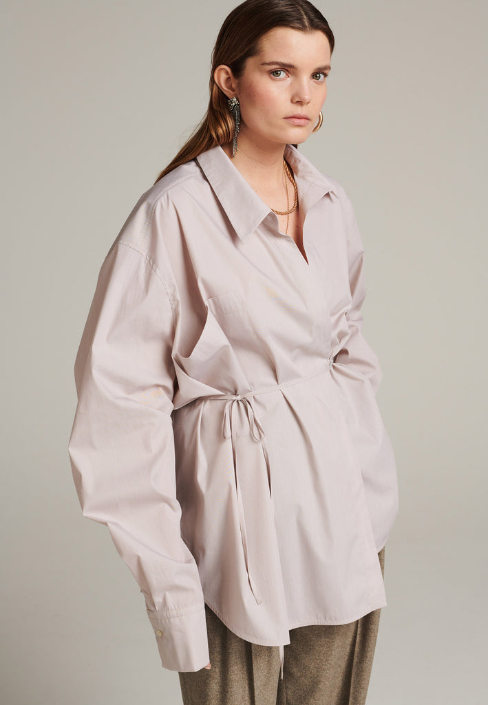 This asymmetric wrapped shirt is made from two different parts sewn together. It's made from 100% cotton poplin in stone, cut for an oversized fit and an unexpected look.
