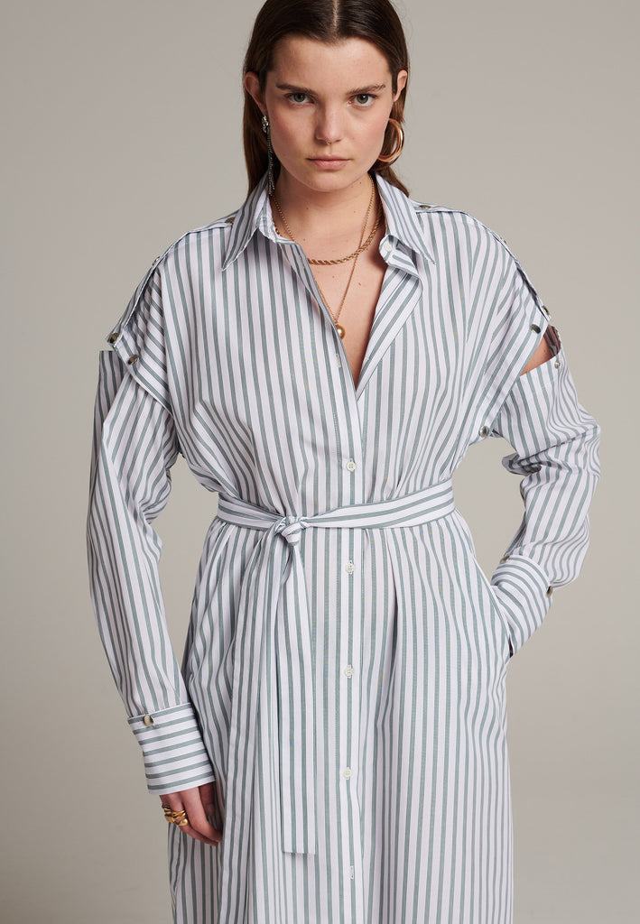 Oversized classic menswear inspred shirt-dress. Cut from 100% crispy poplin cotton in white with dark green thin stripes. Detailed with metal press buttons at the armhole and cuffs to detach the sleeves and cuffs. The back yoke also features press-buttons and you can play with it by opening or closing the cut-out. Designed for a very relaxed fit, use the self-fabric belt to temper the waist.