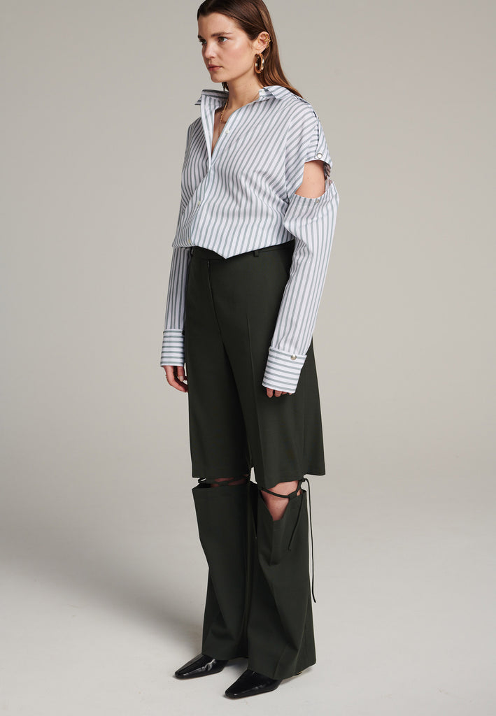 Boyish fitted straight leg trousers cut from fine light wool in black green. Detailed with a cut-out section right below the knee, held to the upper panels by a finely laced string. Can be worn elegantly open, loose or tied together.