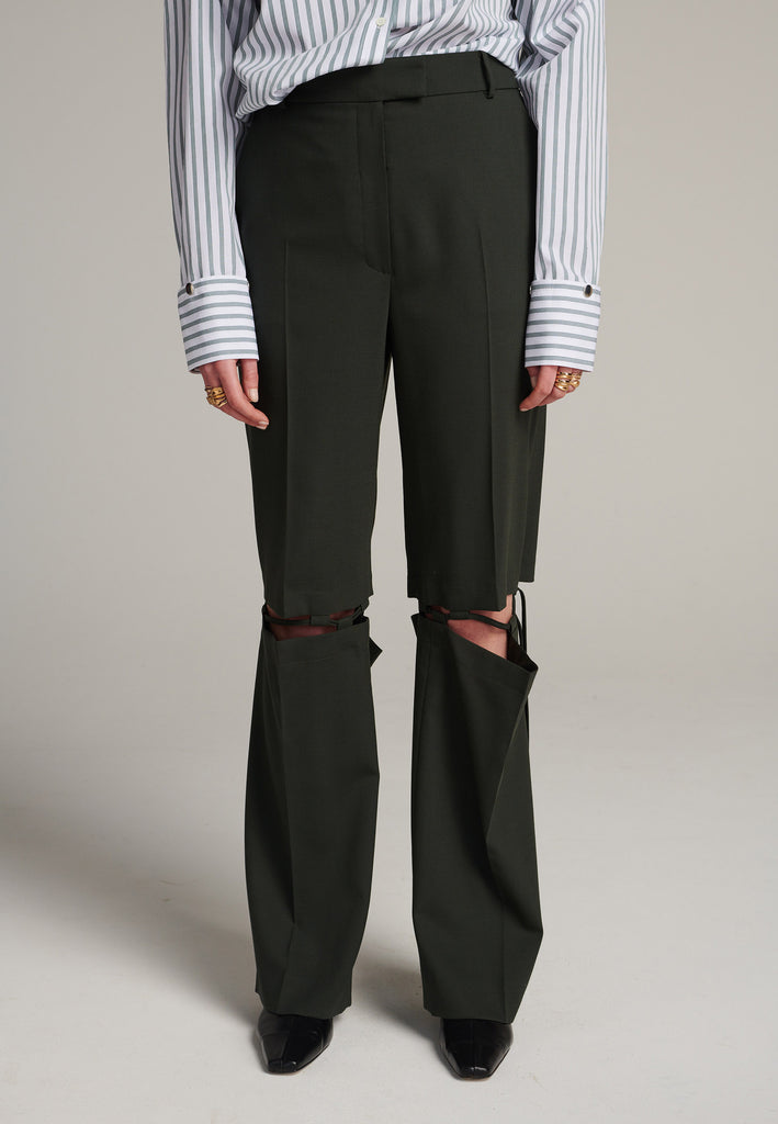 Boyish fitted straight leg trousers cut from fine light wool in black green. Detailed with a cut-out section right below the knee, held to the upper panels by a finely laced string. Can be worn elegantly open, loose or tied together.