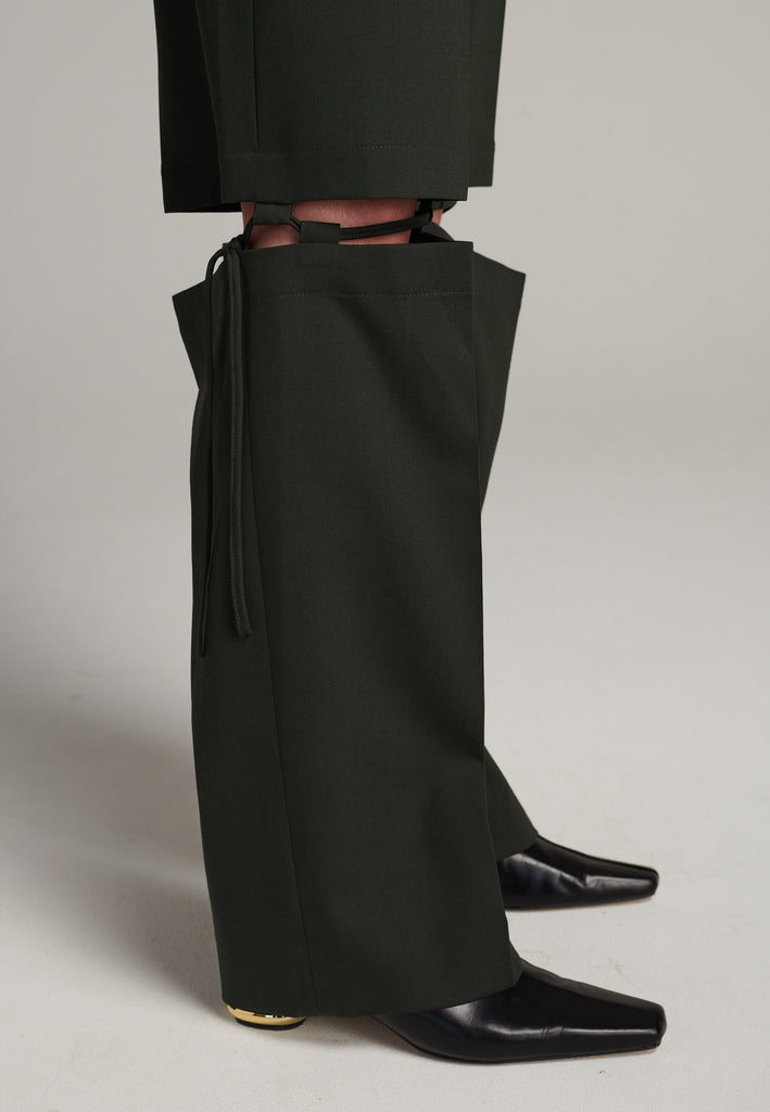 Boyish fitted straight leg trousers cut from fine light wool in black green. Detailed with a cut-out section right below the knee, held to the upper panels by a finely laced string. Can be worn elegantly open, loose or tied together.