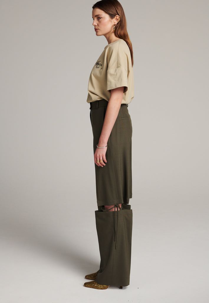 Boyish fitted straight leg trousers cut from fine light wool in dark camel. Detailed with a cut-out section right below the knee, held to the upper panels by a finely laced string. Can be worn elegantly open, loose or tied together.