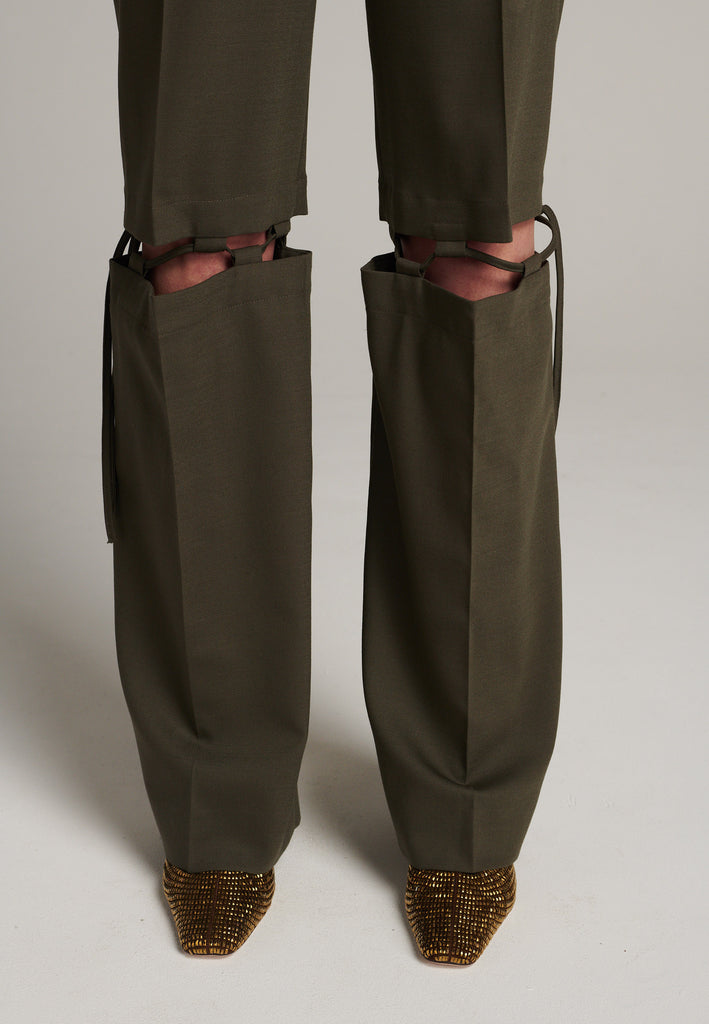 Boyish fitted straight leg trousers cut from fine light wool in dark camel. Detailed with a cut-out section right below the knee, held to the upper panels by a finely laced string. Can be worn elegantly open, loose or tied together.