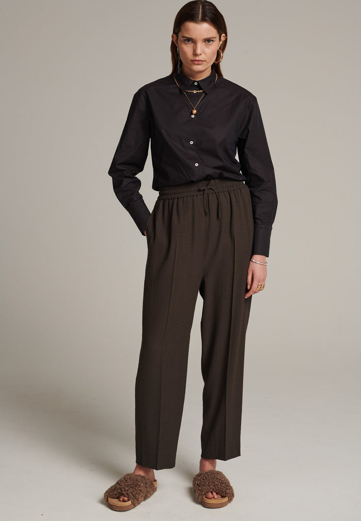 Cropped flowy pants in choco with a high rise. Designed with a loose relaxed fit and drawstring flexible waistband. Pressed front pleat to create a more sophisticated look. Detailed with a welt pocket at the back.