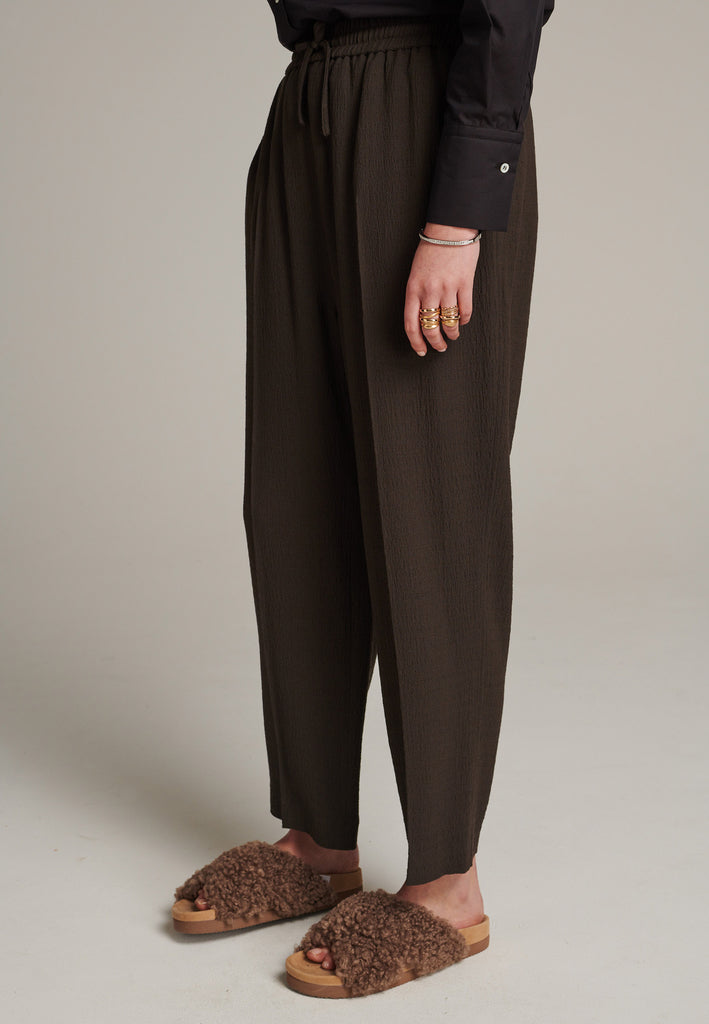 Cropped flowy pants in choco with a high rise. Designed with a loose relaxed fit and drawstring flexible waistband. Pressed front pleat to create a more sophisticated look. Detailed with a welt pocket at the back.