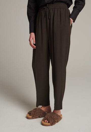 Cropped flowy pants in choco with a high rise. Designed with a loose relaxed fit and drawstring flexible waistband. Pressed front pleat to create a more sophisticated look. Detailed with a welt pocket at the back.