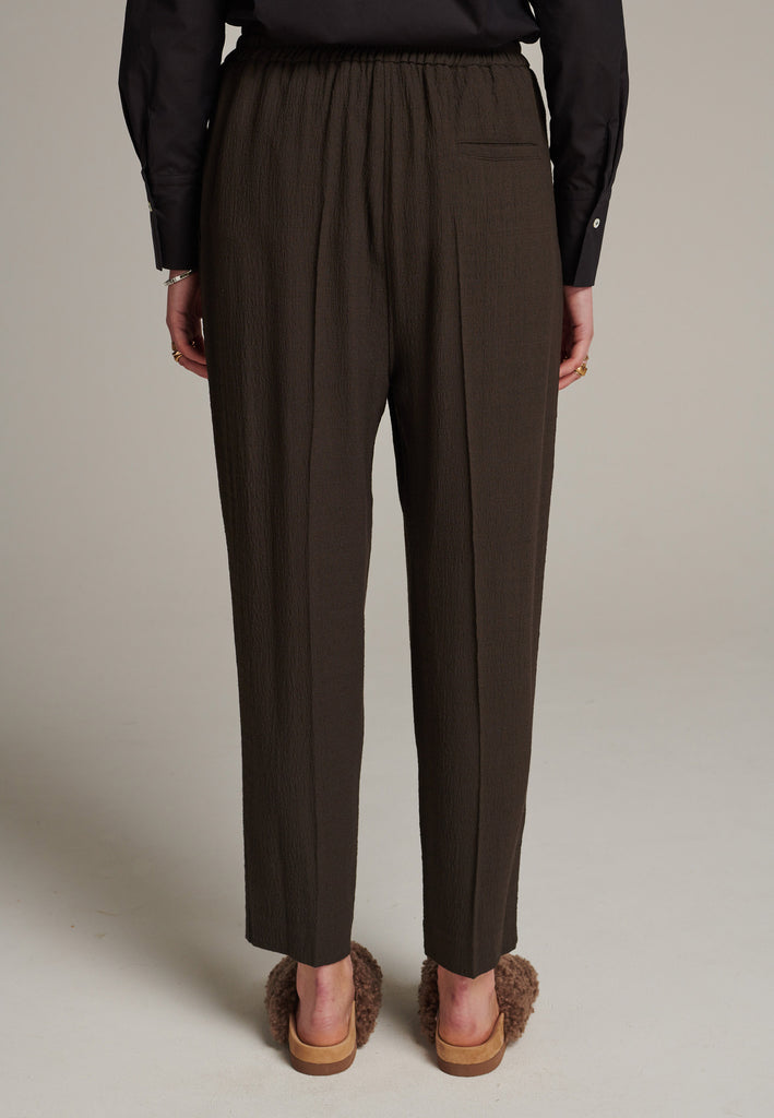 Cropped flowy pants in choco with a high rise. Designed with a loose relaxed fit and drawstring flexible waistband. Pressed front pleat to create a more sophisticated look. Detailed with a welt pocket at the back.
