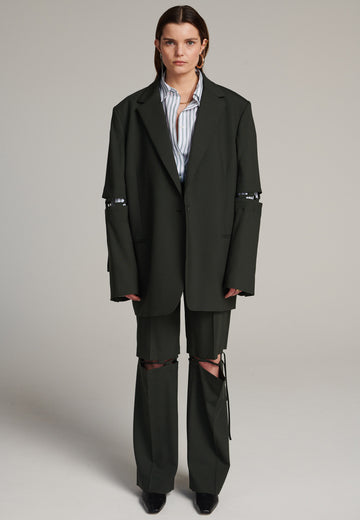 Menswear-inspired smoking blazer in dark green with horn buttons and shoulder pads, emphasizing the oversized fitting. The exaggerated long sleeves can be rolled up to reveal a striped lining. The blazer features a cut-out section around the elbow, making a two-piece sleeve held together by a finely laced string. Can be worn elegantly open, loose or tied together.