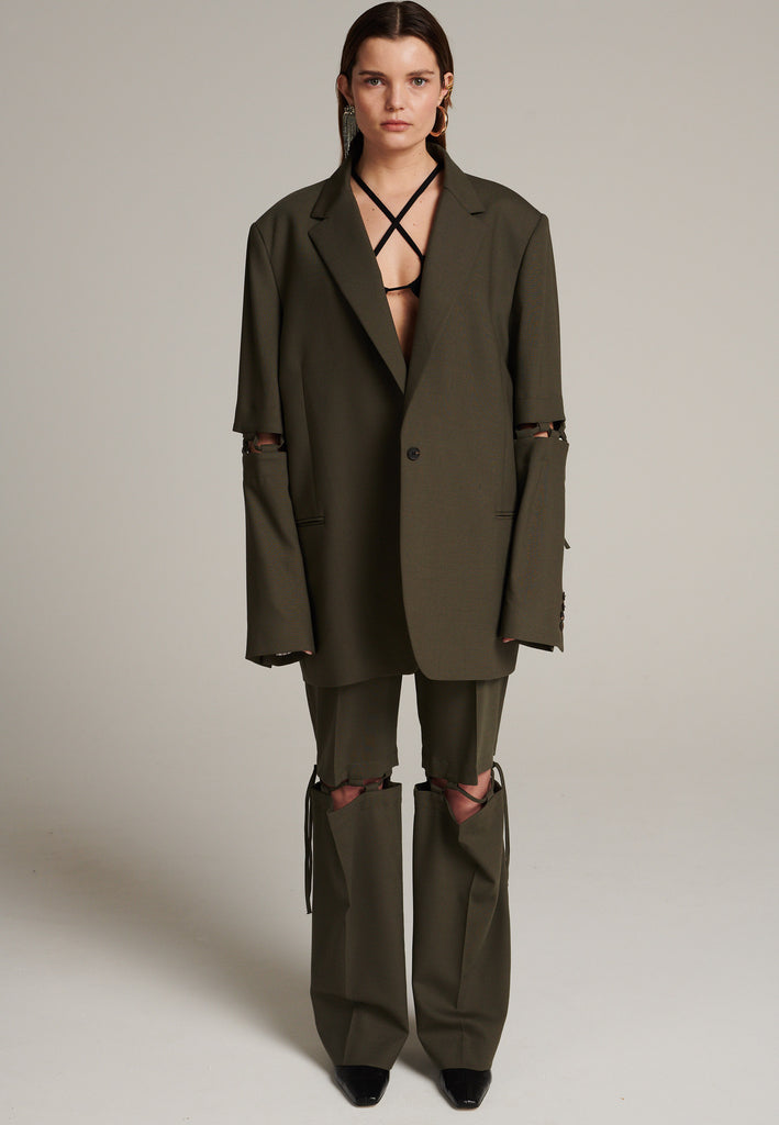 Menswear-inspired smoking blazer in dark camel with horn buttons and shoulder pads, emphasizing the oversized fitting. The exaggerated long sleeves can be rolled up to reveal a striped lining. The blazer features a cut-out section around the elbow, making a two-piece sleeve held together by a finely laced string. Can be worn elegantly open, loose or tied together.