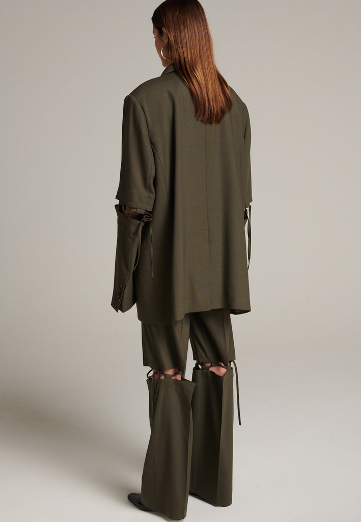 Menswear-inspired smoking blazer in dark camel with horn buttons and shoulder pads, emphasizing the oversized fitting. The exaggerated long sleeves can be rolled up to reveal a striped lining. The blazer features a cut-out section around the elbow, making a two-piece sleeve held together by a finely laced string. Can be worn elegantly open, loose or tied together.