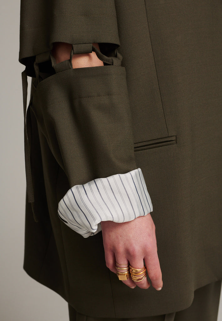 Menswear-inspired smoking blazer in dark camel with horn buttons and shoulder pads, emphasizing the oversized fitting. The exaggerated long sleeves can be rolled up to reveal a striped lining. The blazer features a cut-out section around the elbow, making a two-piece sleeve held together by a finely laced string. Can be worn elegantly open, loose or tied together.