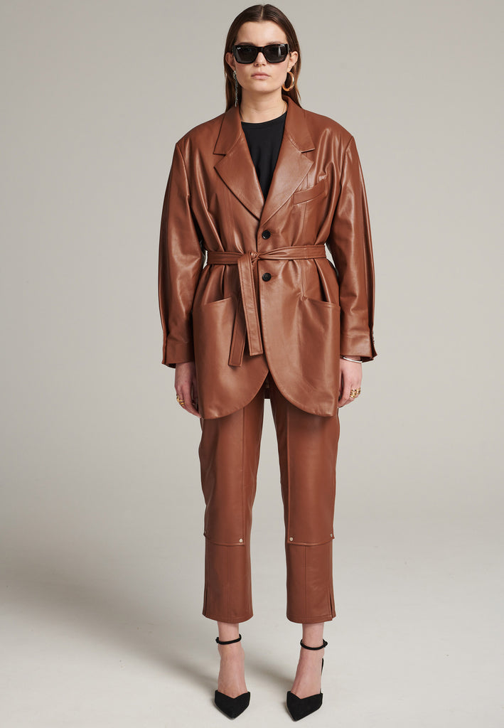 Seasonless oversized leather blazer in cognac with round-shouldered silhouette and coordinating belt that creates some gathering at the back to temper the fitting. Play with it and tie at the smallest part of your waist or tie it at the back for a sense of ease. Pockets, horn buttons and fully lined with. Double fun: wear it as a blazer or as a jacket.