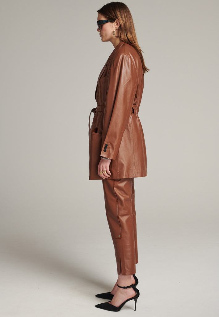 Seasonless oversized leather blazer in cognac with round-shouldered silhouette and coordinating belt that creates some gathering at the back to temper the fitting. Play with it and tie at the smallest part of your waist or tie it at the back for a sense of ease. Pockets, horn buttons and fully lined with. Double fun: wear it as a blazer or as a jacket.