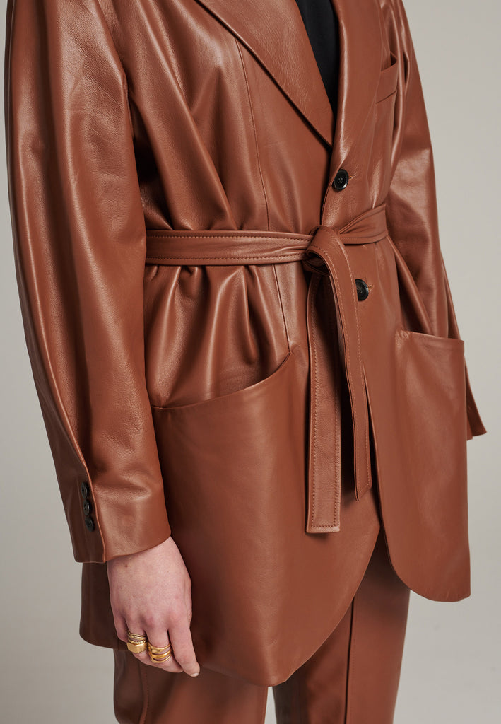 Seasonless oversized leather blazer in cognac with round-shouldered silhouette and coordinating belt that creates some gathering at the back to temper the fitting. Play with it and tie at the smallest part of your waist or tie it at the back for a sense of ease. Pockets, horn buttons and fully lined with. Double fun: wear it as a blazer or as a jacket.